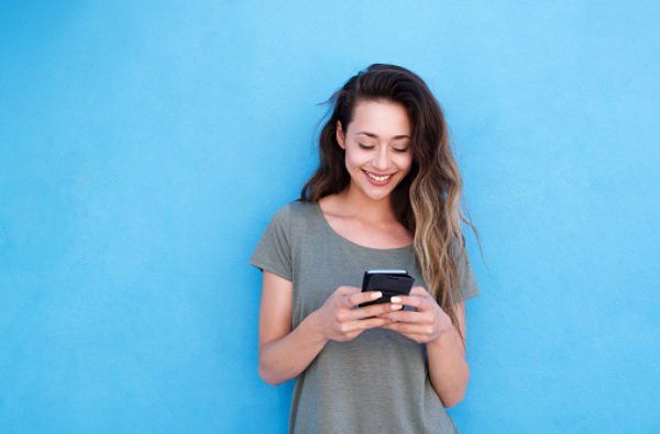 Young smiling woman using mobile phone against blue background