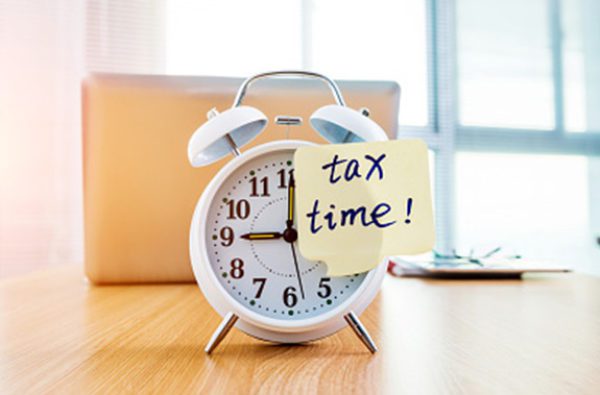 Alarm clock with sticky note reading Tax Time