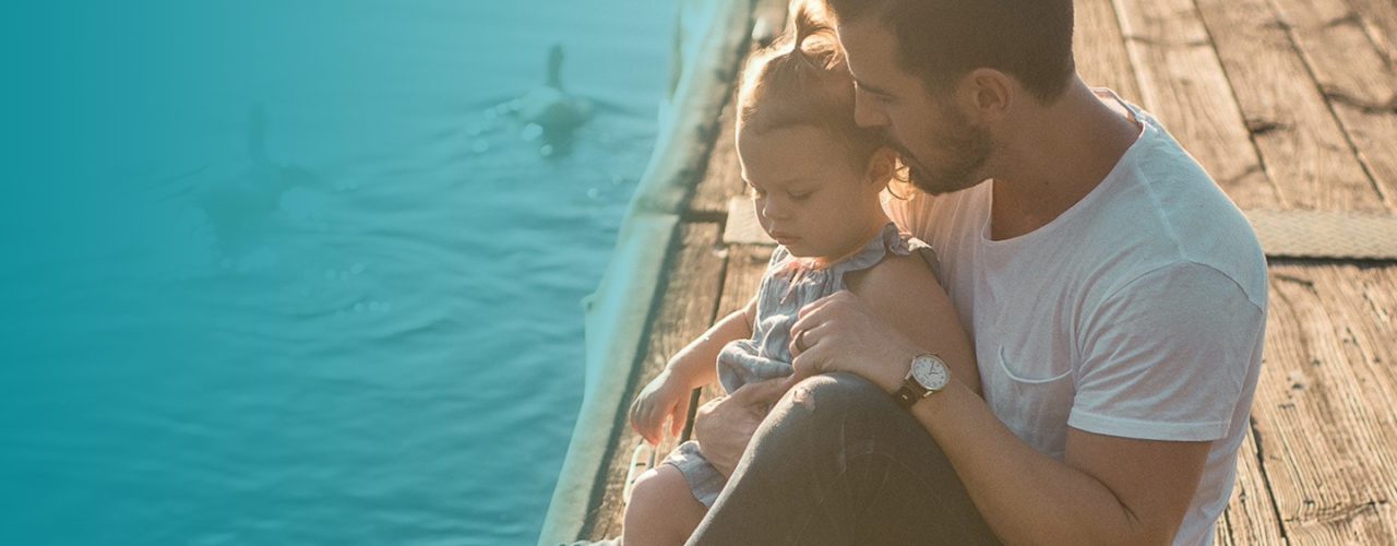 Father holding his daughter while sitting on a dock