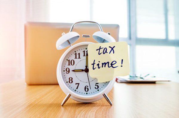 Alarm clock with sticky note reading Tax Time