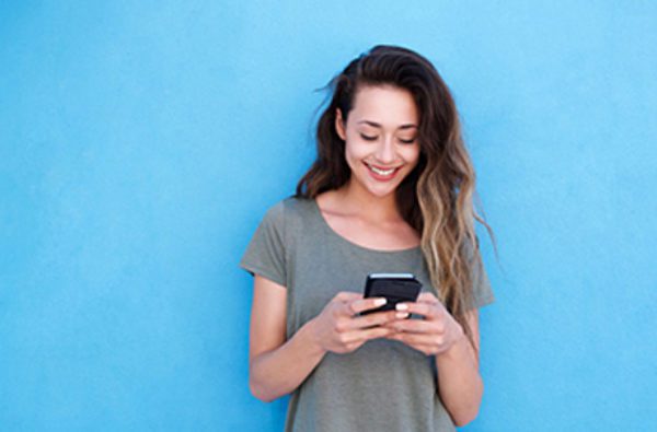 Young smiling woman using mobile phone against blue background