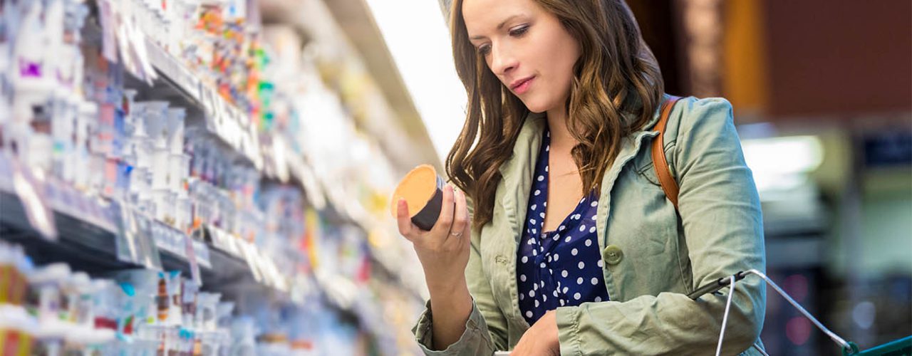 Young lady in a grocery aisle reading price of an item in her hand