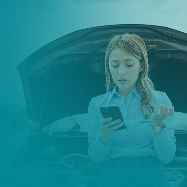 Woman in front of a car with its hood open while she looks at prices on her phone.