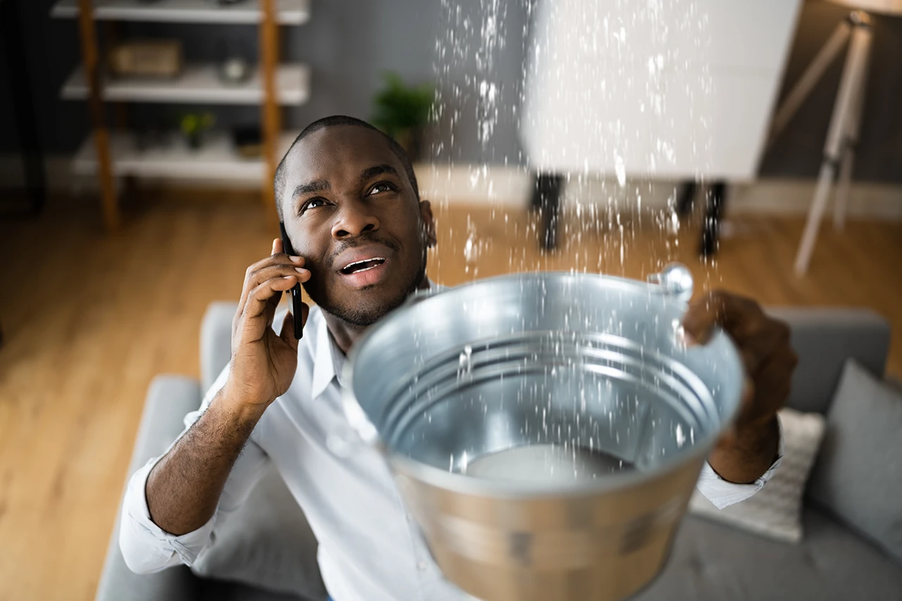 Man calling a plumber while water leaks from the ceiling